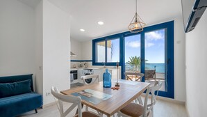 A modern kitchen with white appliances, a dining area with a wooden table and chairs, and a view of the sea through large windows. - Apartment 'Calafellmar Loft' with Sea View, Wi-Fi and Air Conditioning (Calafell)