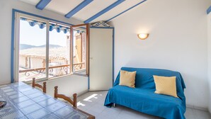 A room with a balcony, a table with chairs, a blue sofa with cushions, and a wall-mounted light fixture. - "Le Zini" Apartment with Sea View, Wi-Fi, and Air Conditioning (Appietto)