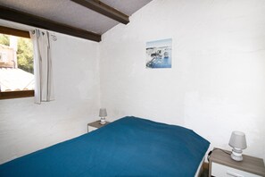 Un dormitorio con una cama, una mesita de noche, una lámpara, una ventana con cortinas y un cuadro colgado en la pared.