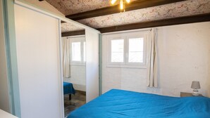 A bedroom with a bed, a wardrobe, a window with curtains, and a nightstand with a lamp.