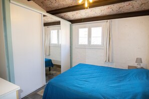 Un dormitorio con cama, armario, ventana con cortinas y mesita de noche con lámpara.