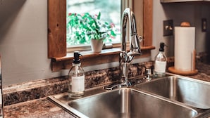 A kitchen with a stainless steel sink, a faucet, a dish soap dispenser, and a window with a view of greenery.