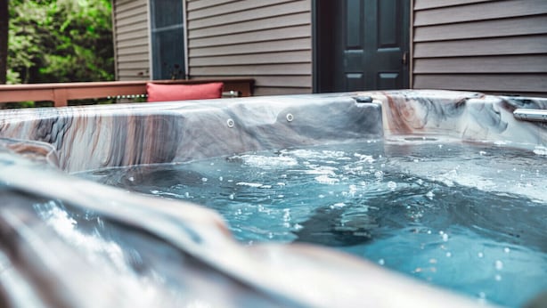 A hot tub with a marble interior, located outdoors in front of a house with a door and window.