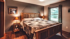 A bedroom with a wooden bed, two bedside lamps, a framed picture on the wall, and a window with curtains.