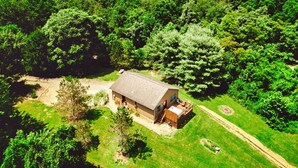 An aerial view of a single-story house with a deck, surrounded by dense green trees and a clear sky. - Romantic Cabin | King Bed | Hot Tub | Spring Vibes (Rockbridge)