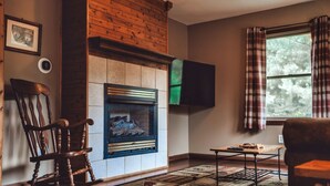 A cozy living room with a fireplace, a television mounted on the wall, and a window with curtains. - Romantic Cabin | King Bed | Hot Tub | Spring Vibes (Rockbridge)