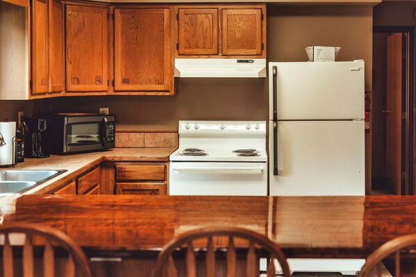 A kitchen with wooden cabinets, a white stove, a white refrigerator, a microwave, and a sink.