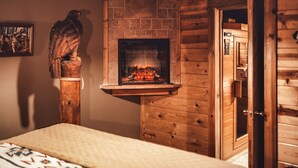 A cozy room with a fireplace, wooden walls, and a bed with a patterned bedspread. - Romantic Cabin | Private Stay | King Bed | Fire Pit (Rockbridge)
