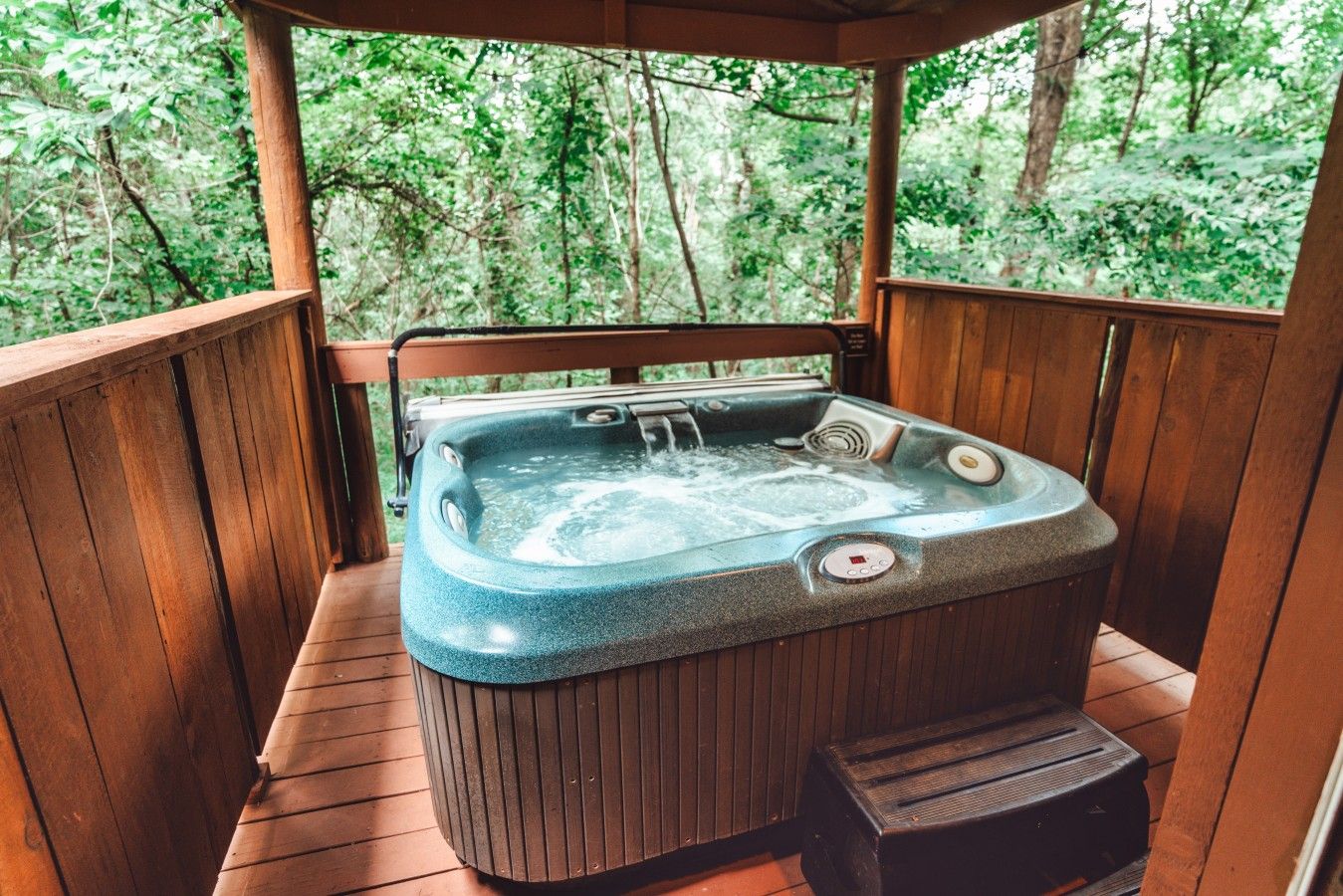 Ein Whirlpool auf einer Holzterrasse mit Blick auf einen Wald.