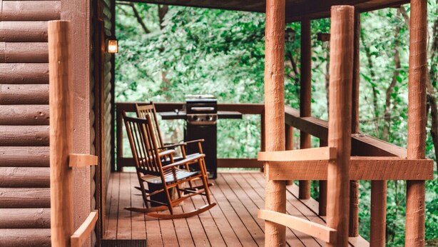 A wooden deck with a rocking chair and a grill, surrounded by lush greenery. - Romantic Cabin | Private Stay | King Bed | Fire Pit (Rockbridge)
