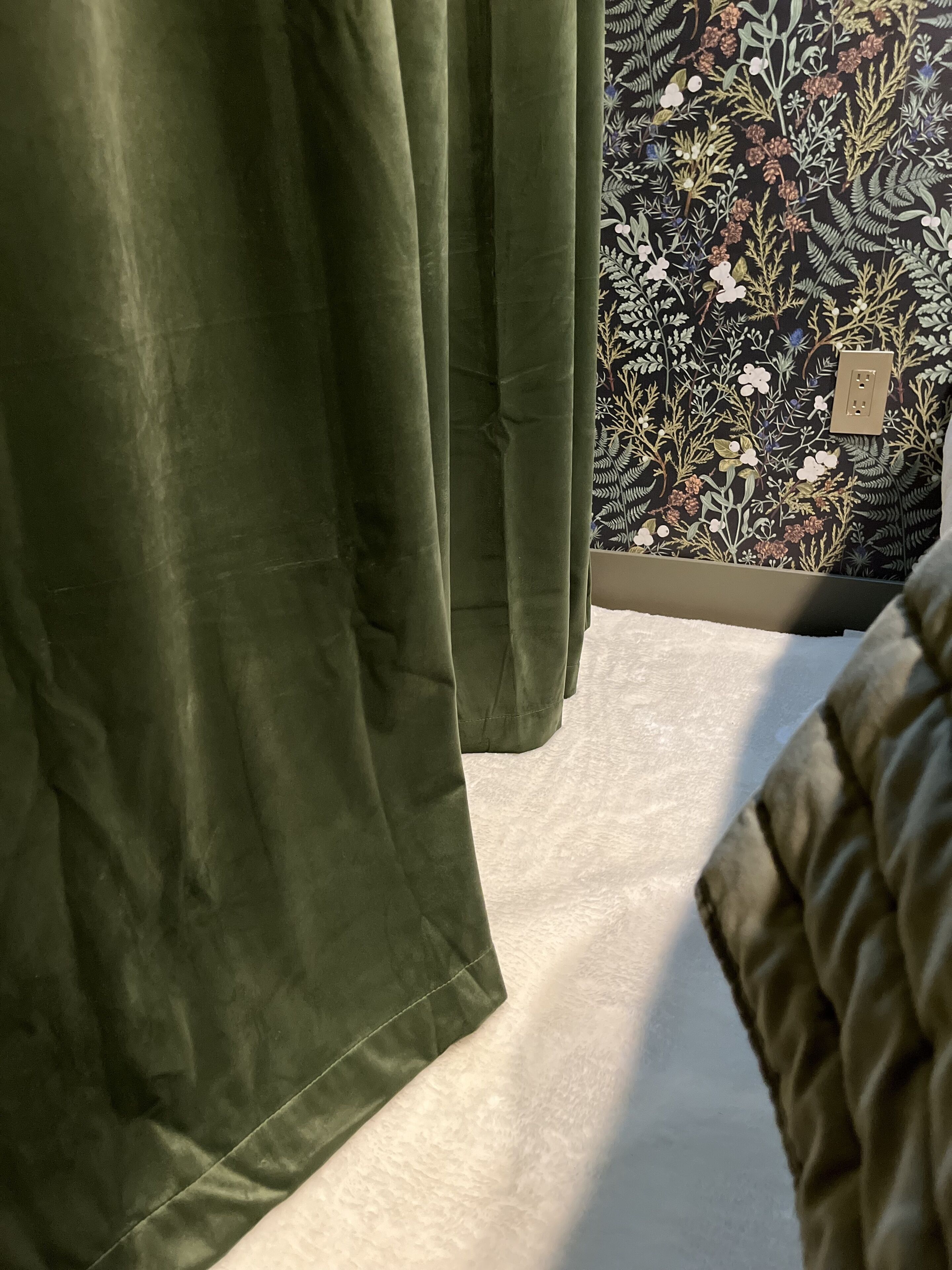 Quarto com cortina verde, papel de parede estampado e carpete branco.
