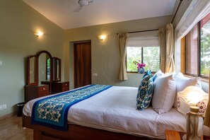 A bedroom with a bed, a dresser, a mirror, a window with curtains, and a ceiling fan. - Dulwich Park View, Panchgani - Amã Stays & Trails  (Mahabaleshwar)