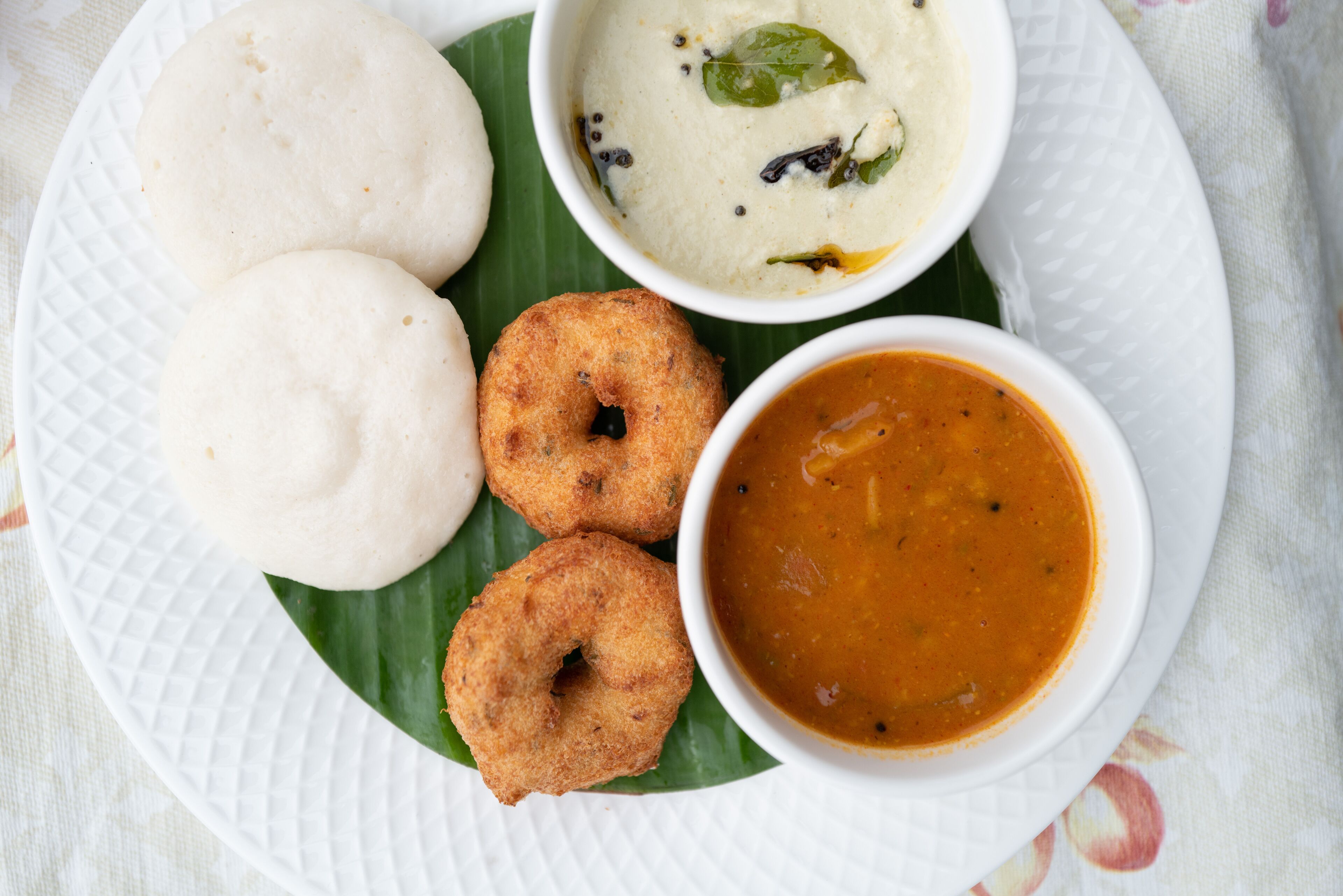 Une assiette contenant deux idlis, deux vadas et deux bols de sambar et de chutney à la noix de coco.
