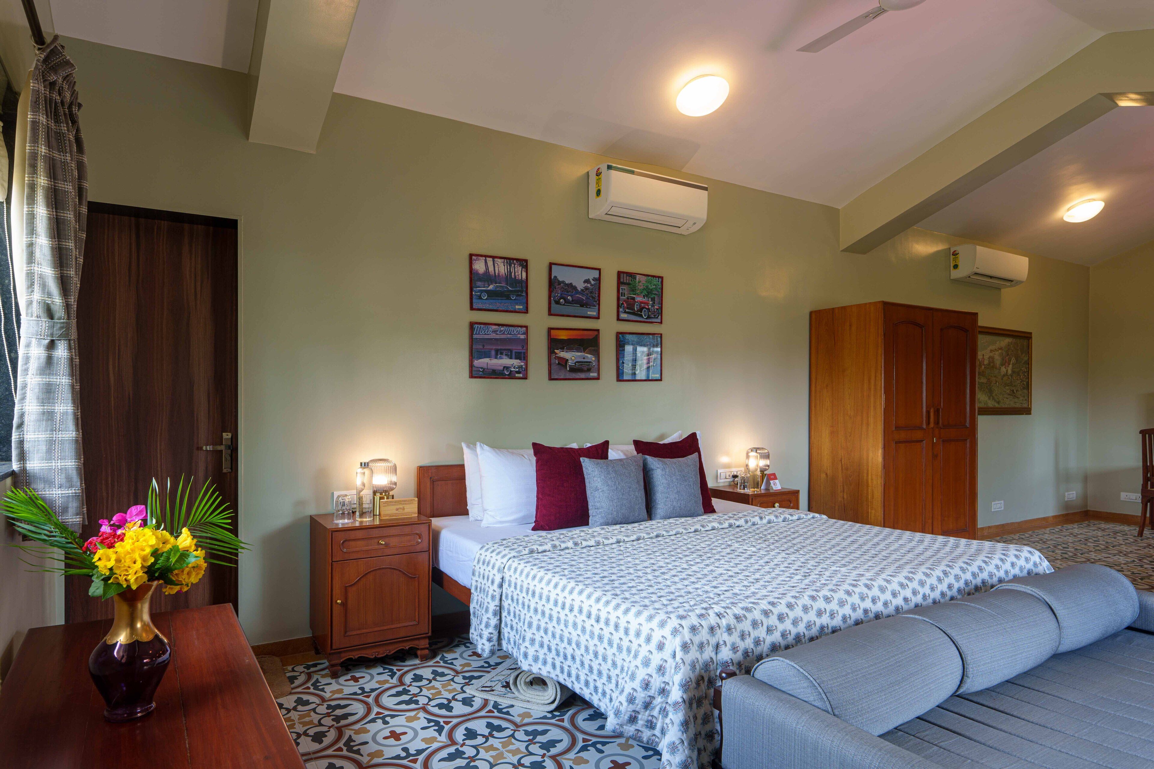 A bedroom with a bed, bedside tables, a dresser, an air conditioner, and framed pictures on the wall.