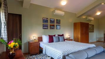 A bedroom with a bed, bedside tables, a dresser, an air conditioner, and framed pictures on the wall.