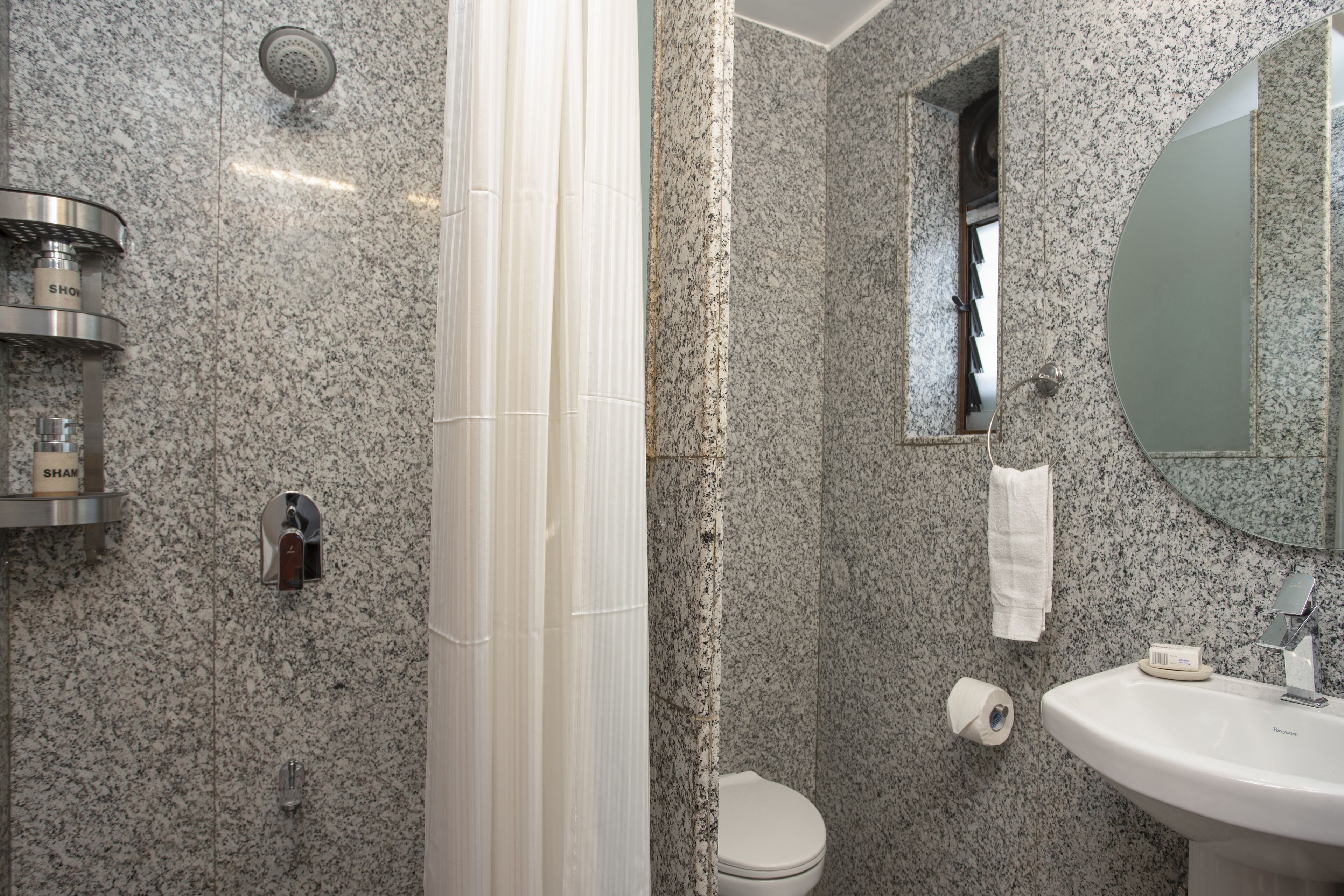 Un baño con pared de granito, ducha, inodoro, lavamanos y espejo.