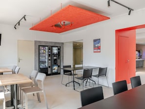 A modern interior with a meeting table, chairs, a vending machine, and a red accent wall. - ibis budget Bordeaux Sud Villenave-d'Ornon (Villenave-d'Ornon)