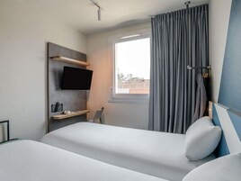 Habitación de hotel con cama, televisor montado, ventana con cortinas y vistas al exterior.