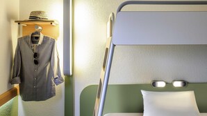 A bunk bed with a pillow and a hanging garment rack with a hat and shirt.