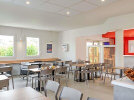 Un área de comedor moderna con varias mesas y sillas, una barra con productos horneados y amplias ventanas que dejan entrar luz natural.