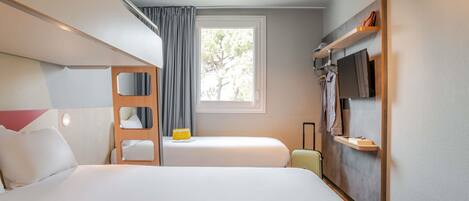Een hotelkamer met een stapelbed, een enkel bed, een raam met gordijnen, een televisie en een klein tafeltje met een koffer.