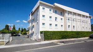 A modern white building with multiple floors, a staircase on the left, and a gated entrance.