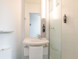 Un baño con lavamanos blanco, espejo, toalla y zona de ducha.