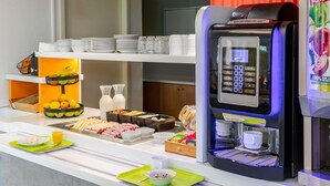 A buffet setup with a coffee machine, various food items, and a beverage dispenser. - ibis budget Bordeaux Sud Villenave-d'Ornon (Villenave-d'Ornon)