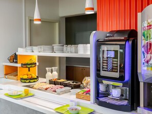 Montaje tipo bufé con una máquina de café, diferentes opciones de comida y un dispensador de bebidas.