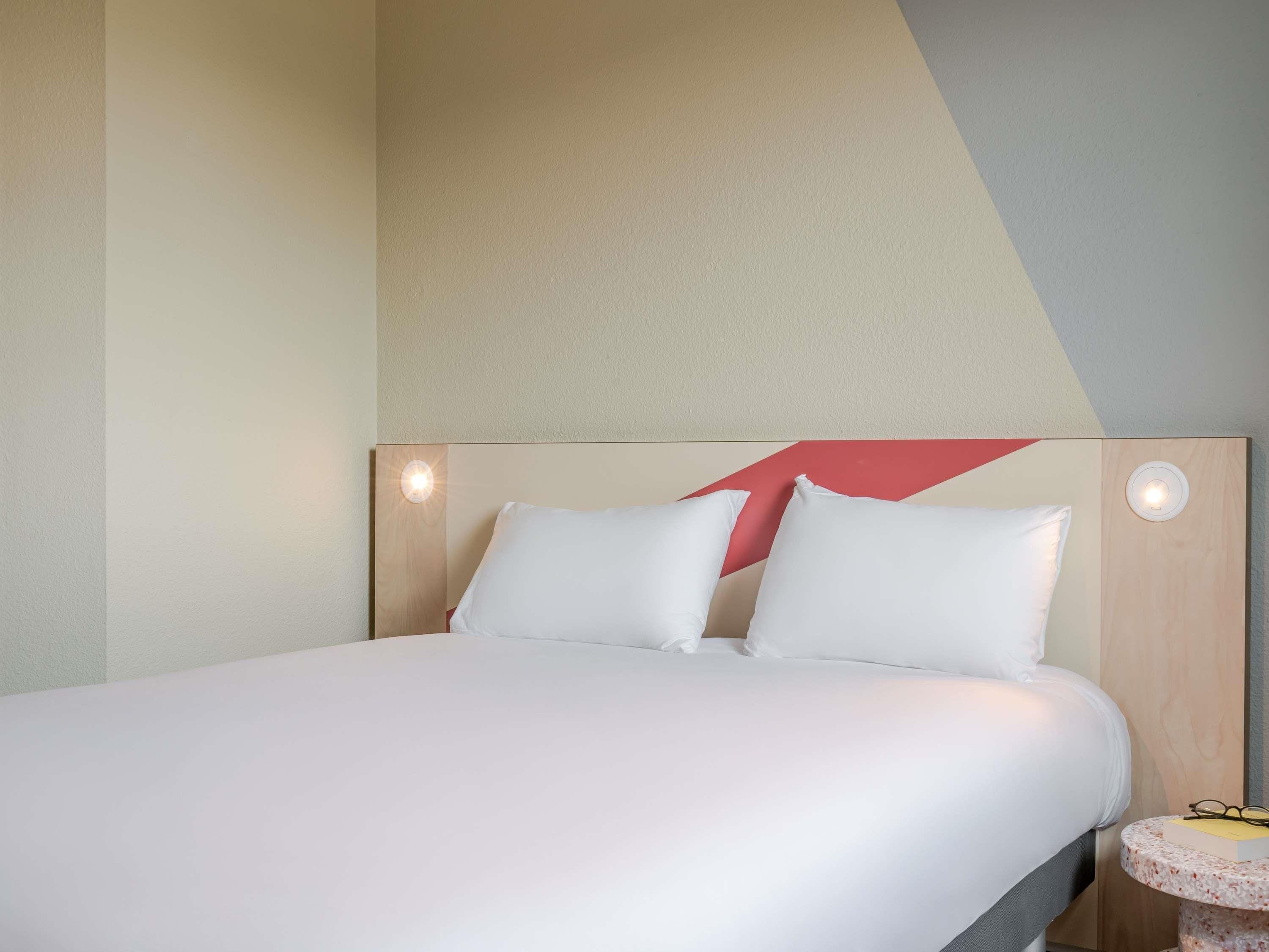 A hotel room with a bed, pillows, a nightstand, and a wall with a geometric design.