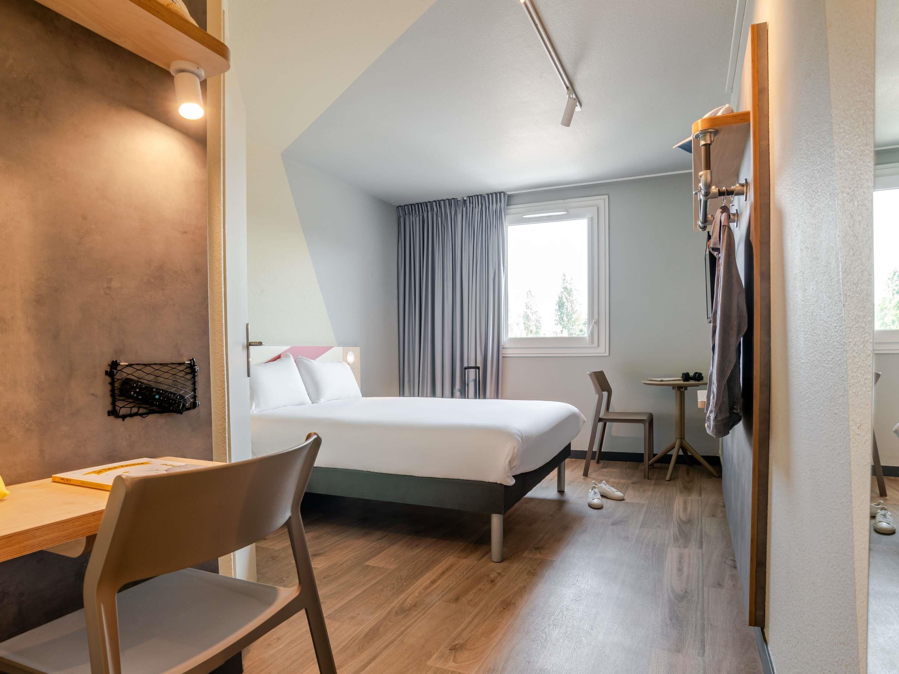 Een hotelkamer met een bed, een bureau, een stoel, een televisie en een raam met gordijnen.