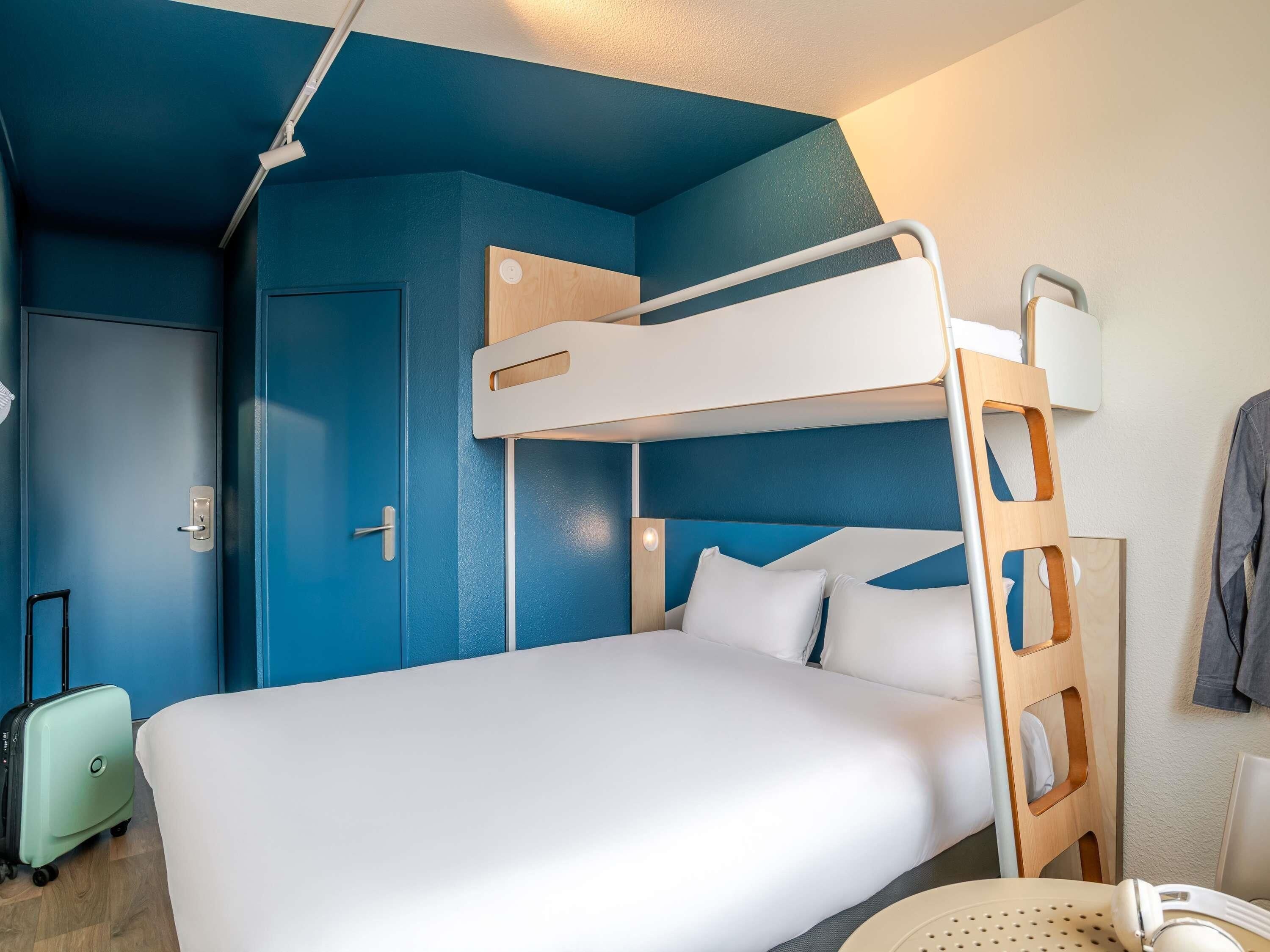 Una cama litera con escalera, una maleta y una mesa redonda con una silla.
