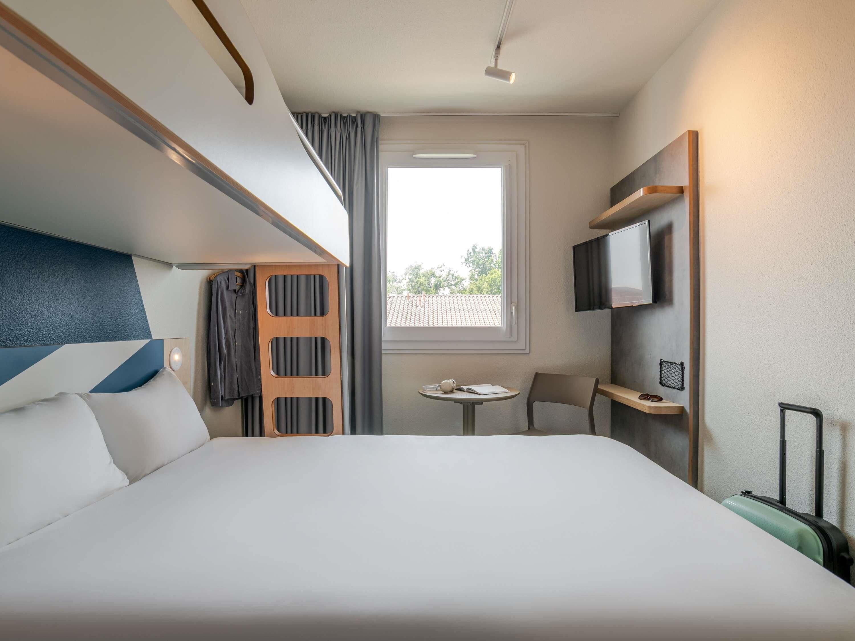 Ein Hotelzimmer mit Bett, Fernseher, kleinem Tisch und Fenster.