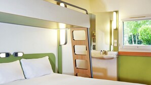 A hotel room with a bed, a bathroom with a sink and mirror, and a window with a view of greenery.