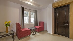 A room with two red upholstered chairs, a small glass table, a wooden door, and a window with curtains. - Itsy Hotels Peak View, 300 Mts From Mall Road (Mussoorie)