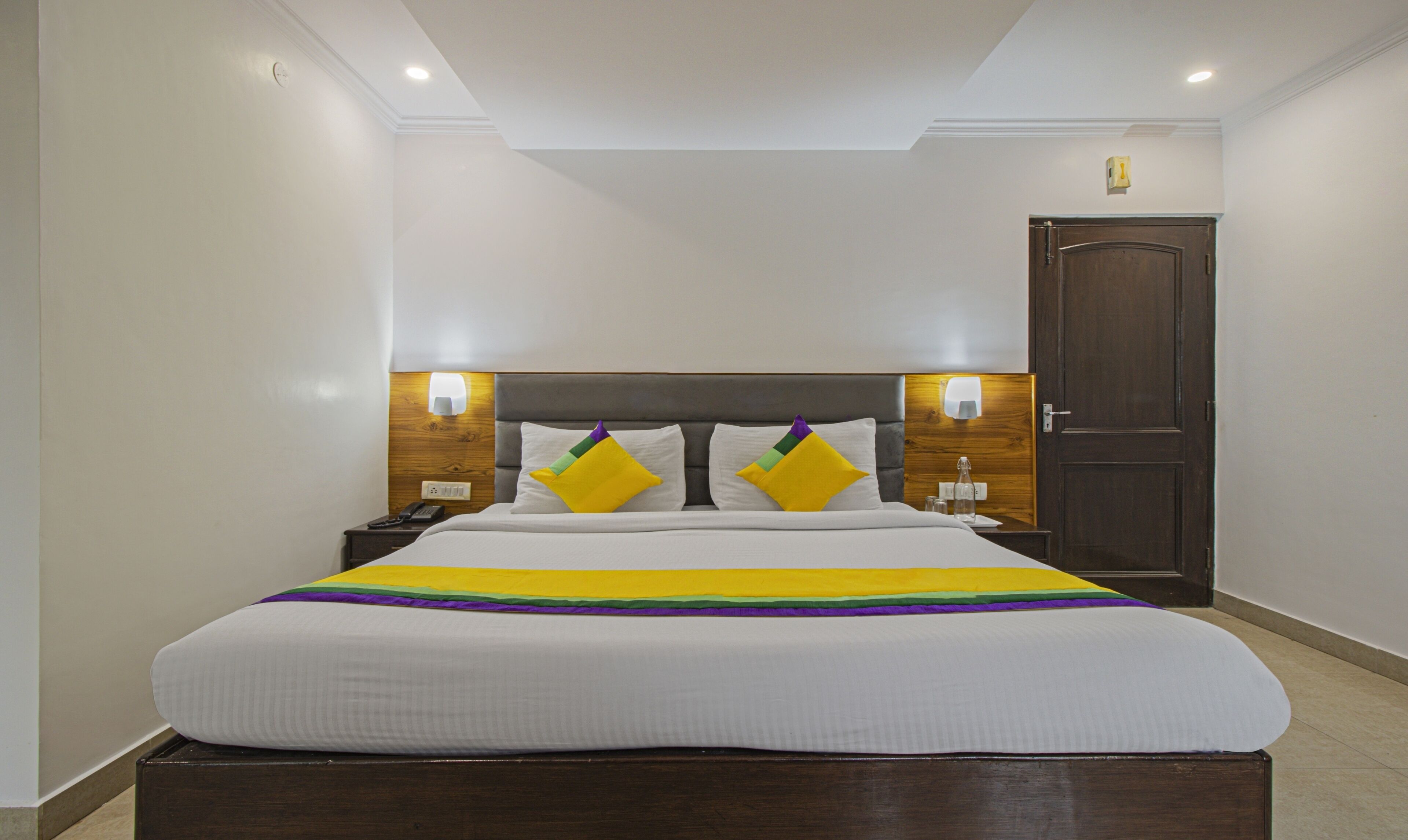 Habitación de hotel con una cama grande, cabecero de madera, lámparas de noche y una puerta.