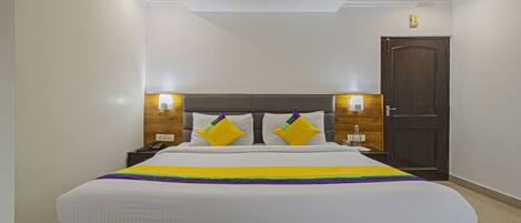 Habitación de hotel con una cama grande, cabecero de madera, lámparas de noche y una puerta.