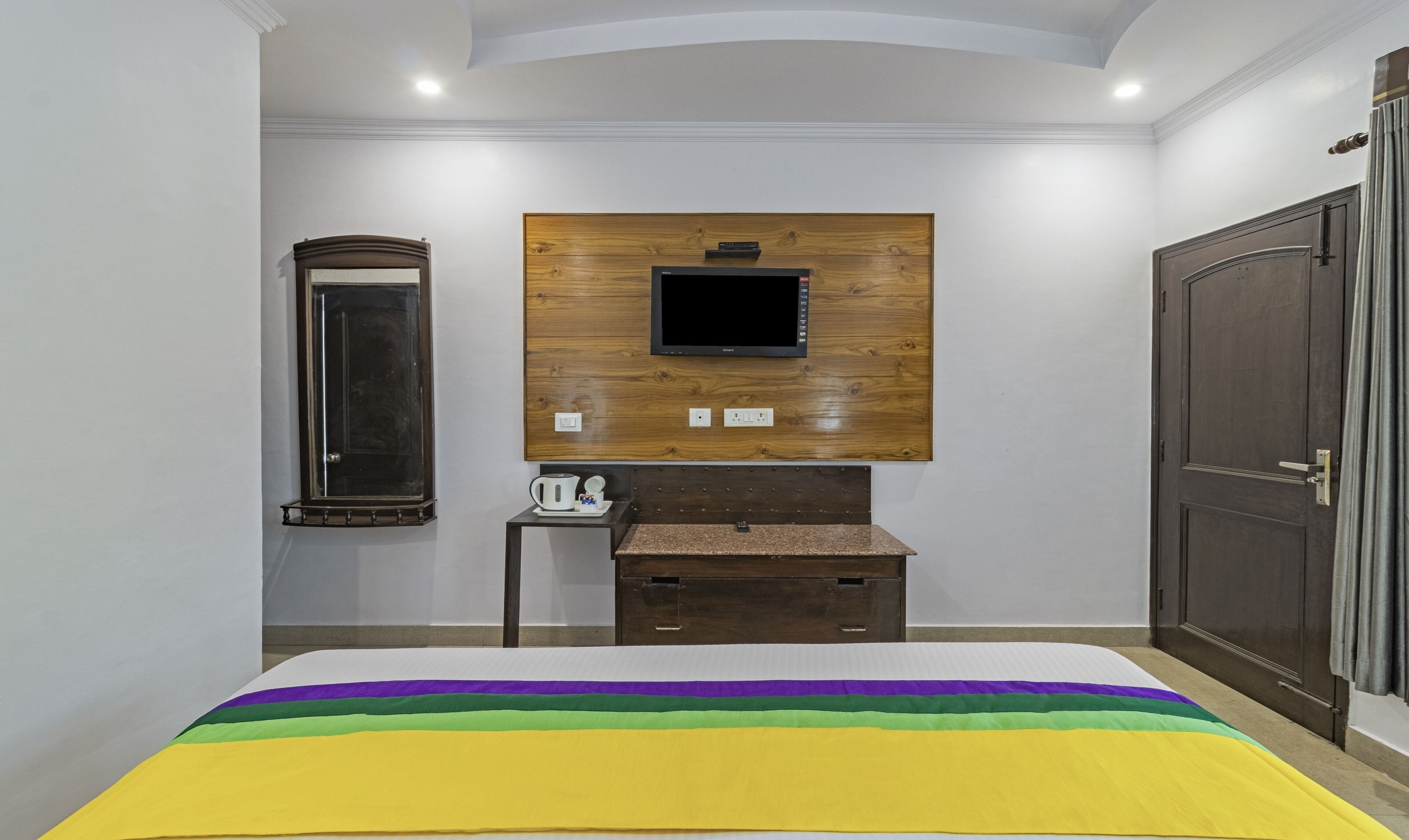 A hotel room with a bed, a wooden panel wall, a television, a mirror, and a wardrobe.