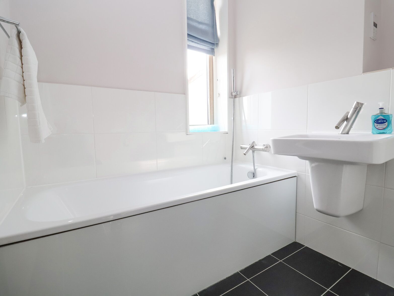 A modern bathroom with a white bathtub, a sink, and a window with a blue blind.