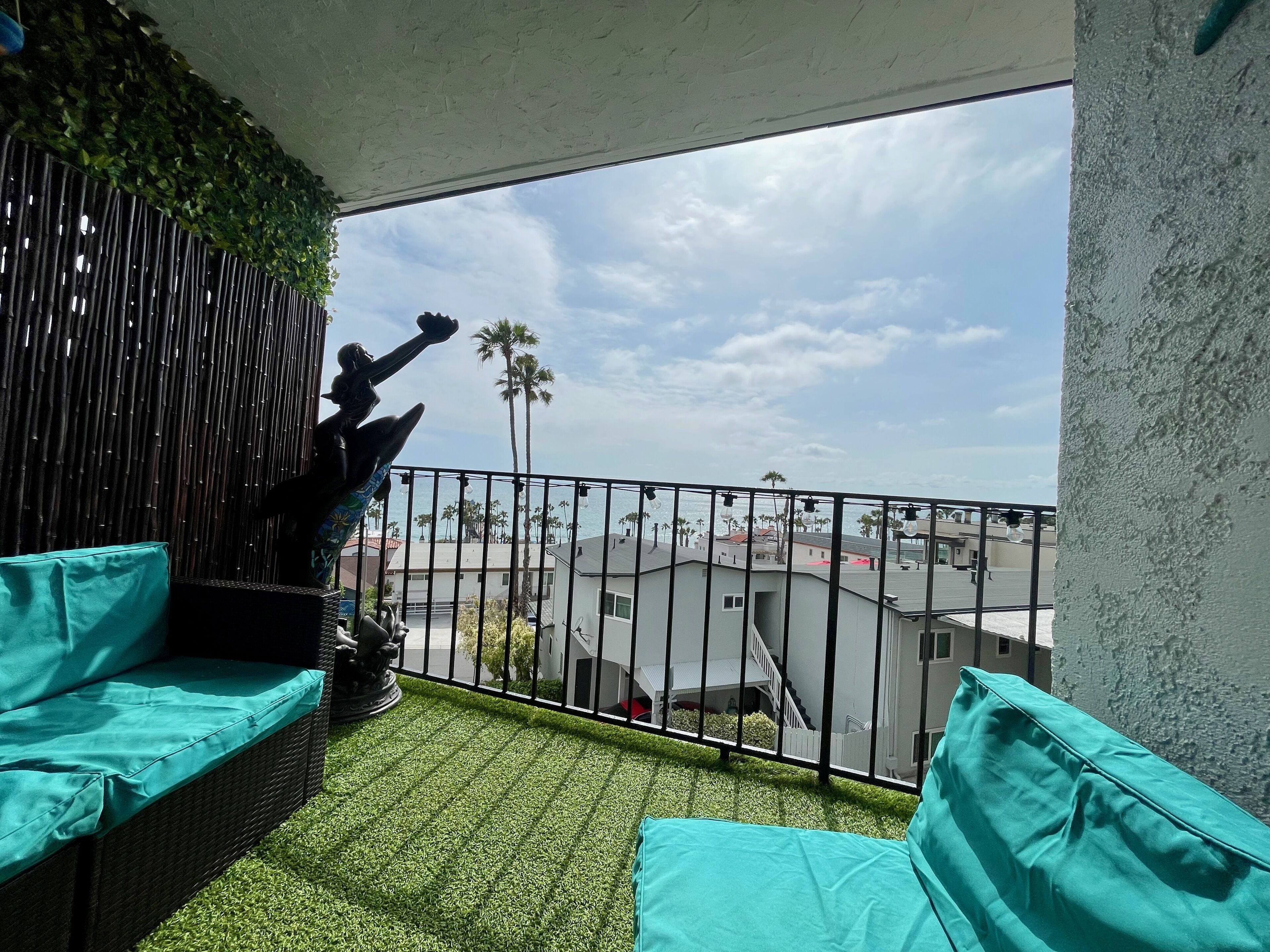 A balcony with artificial grass, a wicker sofa, and a decorative wall.