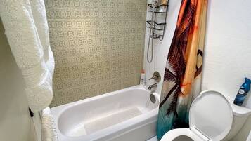 A bathroom with a bathtub, toilet, shower, and patterned tiles.