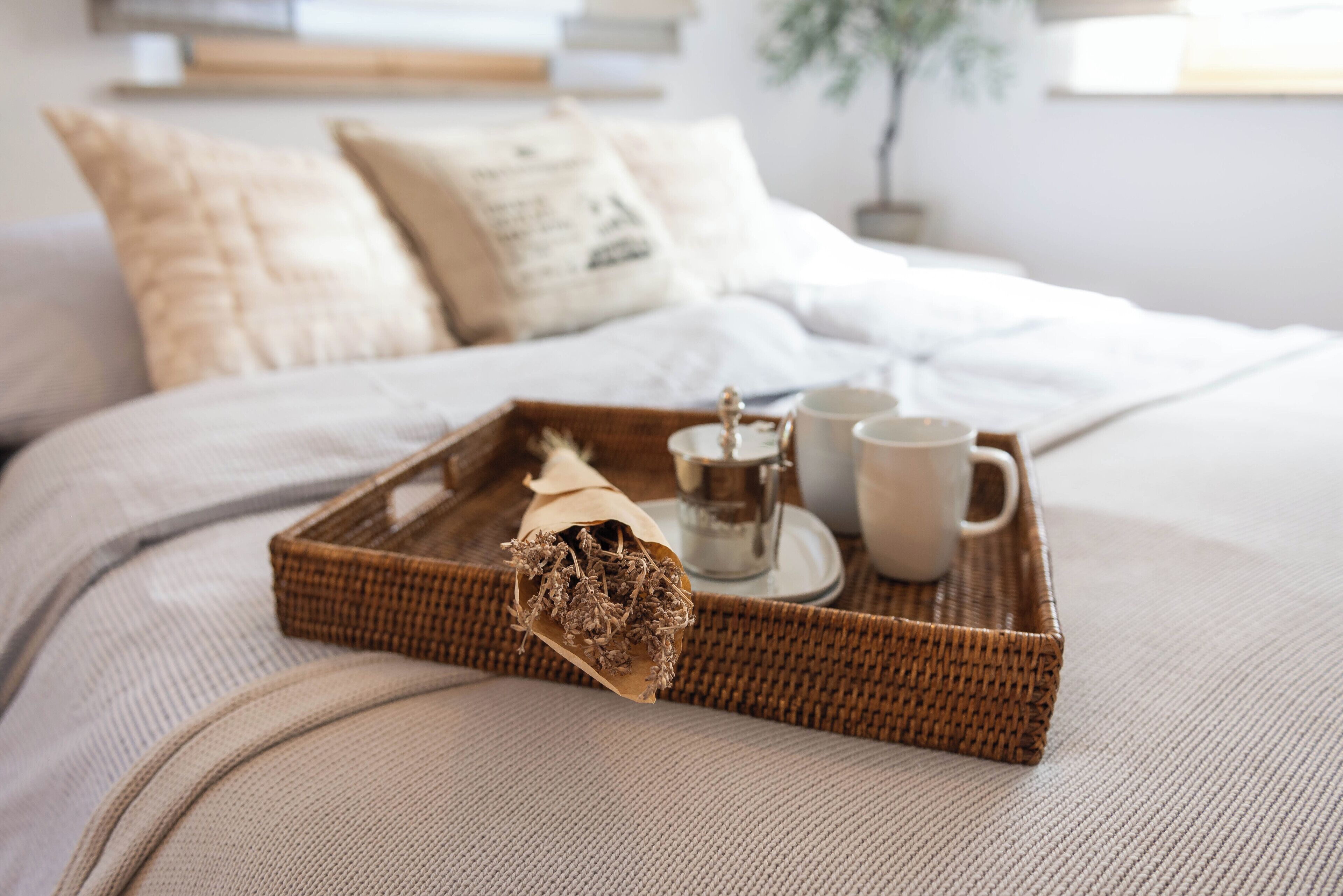 Una cama bien hecha con una bandeja que contiene una tetera, dos tazas y un trozo de planta seca.