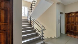 A staircase with a modern design, a wooden door on the left, and a door with a number plate on the right. - Treebo Dreams Arcade (Aluva)
