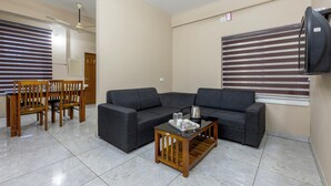 A living room with a sofa, a coffee table, and a dining area with chairs and a table. - Treebo Dreams Arcade (Aluva)