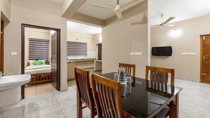 A hotel room with a bed, a bathroom, a dining area with a table and chairs, and a TV mounted on the wall. - Treebo Dreams Arcade (Aluva)