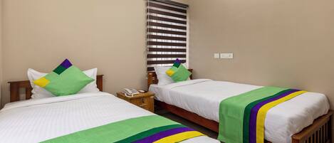 A hotel room with two single beds, each with a striped headboard, a bedside table with a phone, and a wall-mounted air conditioner.