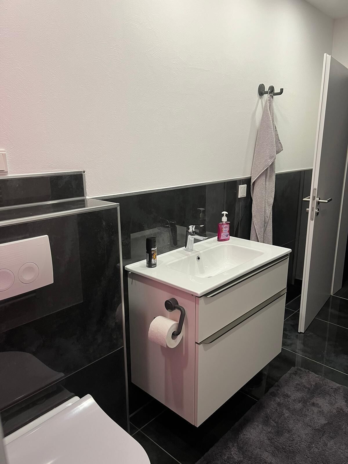 A modern bathroom with a white sink, black and white vanity, a toilet, and a towel hanging on a hook.