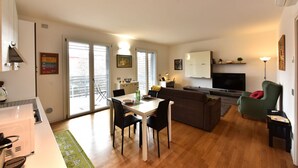 A modern living room with a dining area, a sofa, a TV, and a kitchen area. - GuestHost - Casa Kikka: luminoso bilo con balcone (Cernusco sul Naviglio)