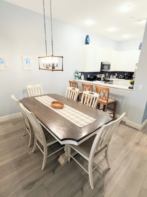 Un comedor con una mesa de madera, sillas blancas y una lámpara colgante.
