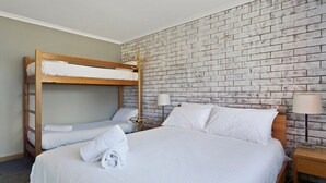Une chambre avec un lit superposé, un lit simple, un mur en briques, une table de chevet avec une lampe et une serviette sur le lit simple.